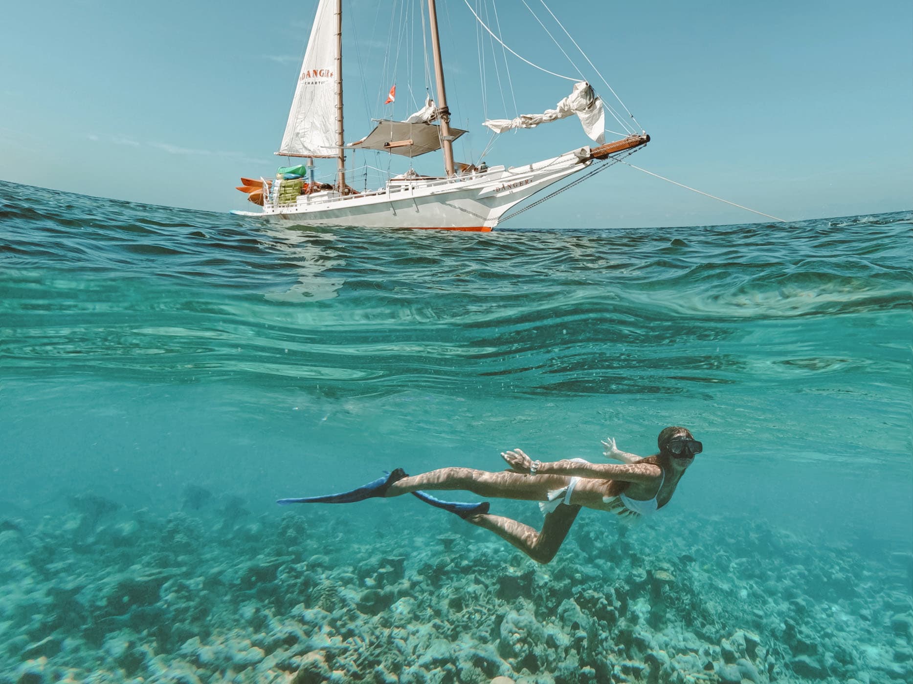 A woman snorkelling with a sail boat in the water